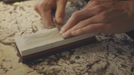 close up of hands sharpening a small knife with whetstone