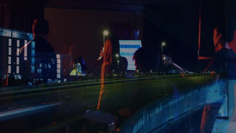 band performing live music on stage through reflective window, overlaying mic and car light trails