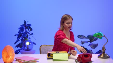 a focused woman in a red dress talks on a red rotary phone while organizing pastel sheets on her desk. surrounded by a typewriter and colorful lamps, she works in a nostalgic retro office setup