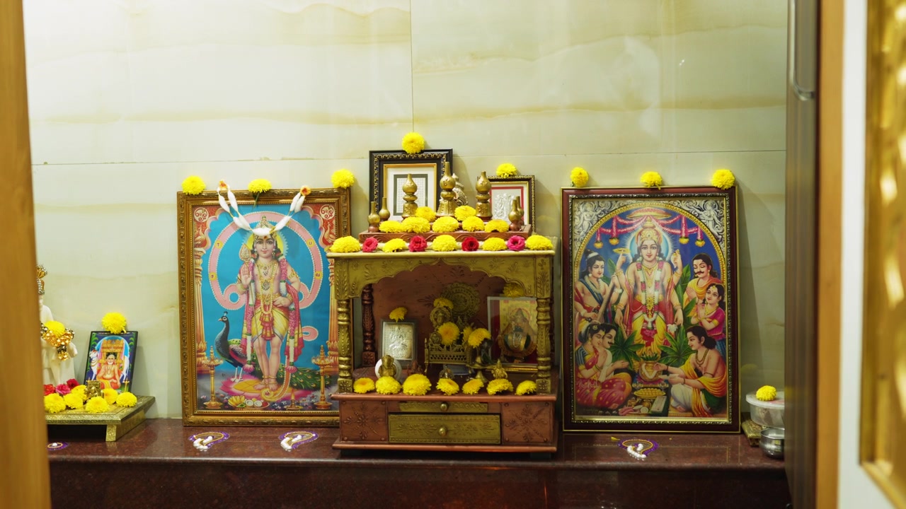 Santuario della sala pooja dell'India meridionale con divinità incorniciate e fiori di calendula gialli disposti ordinatamente sull'altare al rallentatore