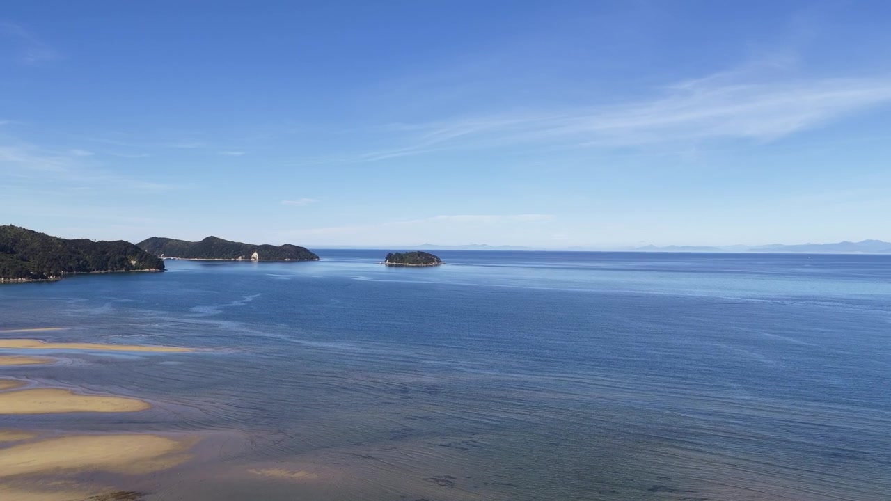 Riprese aeree con drone di una costa oceanica limpida e blu con onde leggere e spiaggia sabbiosa sotto un cielo azzurro brillante in Nuova Zelanda