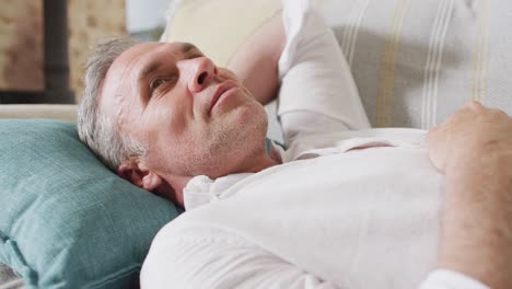 happy caucasian man lying on sofa in living room and smiling