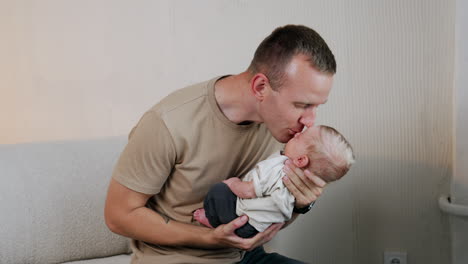 caucasian mid-aged man holding his tiny newborn baby. father kisses his son and talk to him smiling.