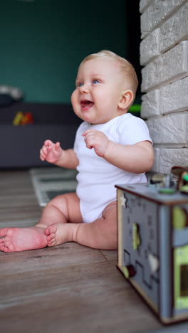 lovely joyful baby boy wearing white bodysuit sits on the floor dancing. cute child's portrait playing at home. vertical video.