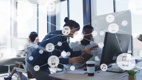 animation of connected icons over diverse coworkers discussing reports on desktop at office
