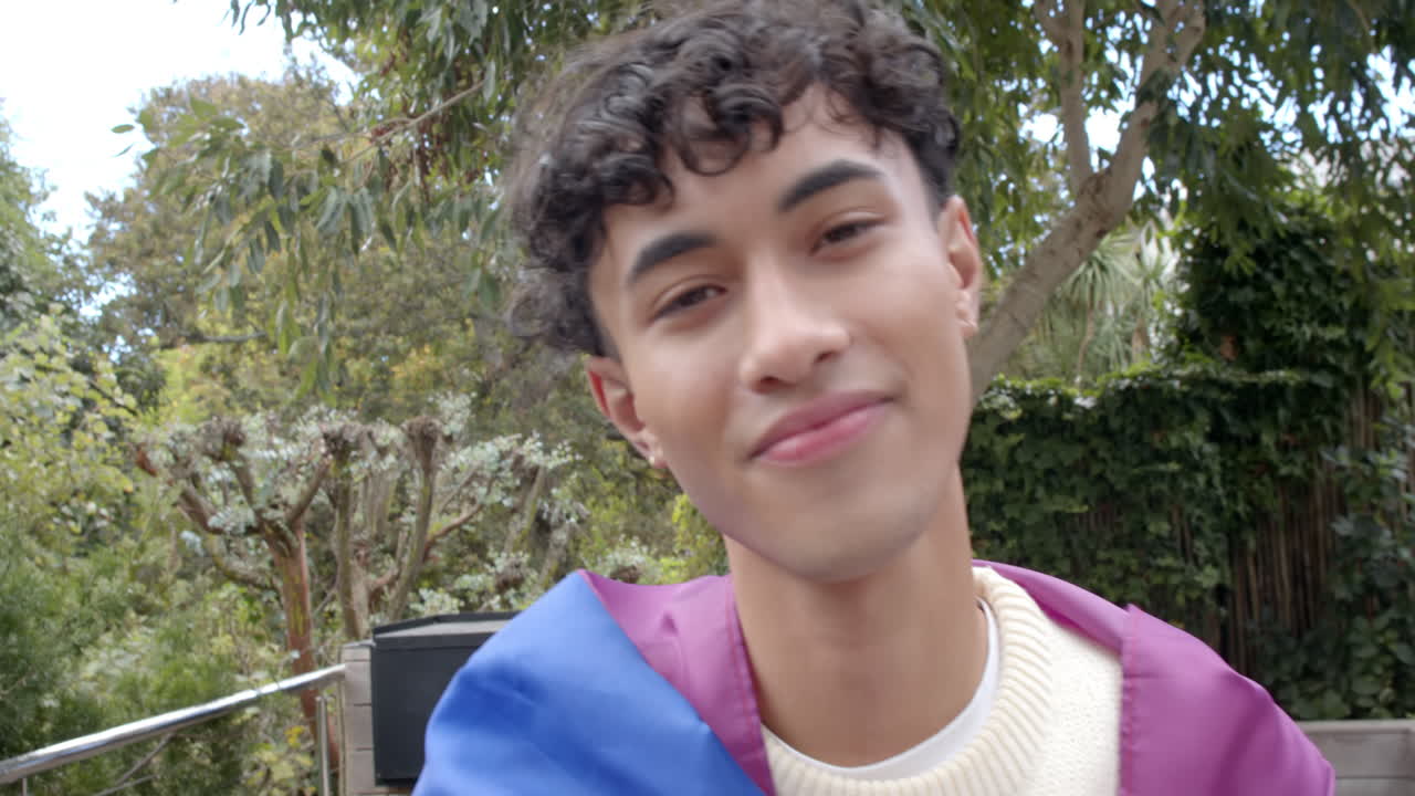 Smiling young man wrapped in pride flag, enjoying peaceful outdoor moment, copy space