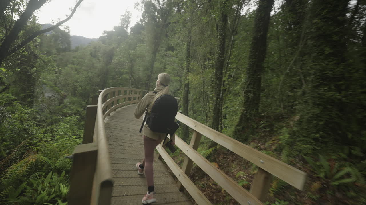 mujer fotógrafa turística visitando el mirador de madera con vistas al río azul hokitika