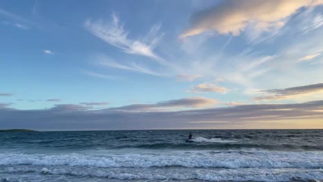 A-silhouette-of-a-man-surfing-with-kite-on-waves-and-jumping-out-of-the-water-in-sunset
