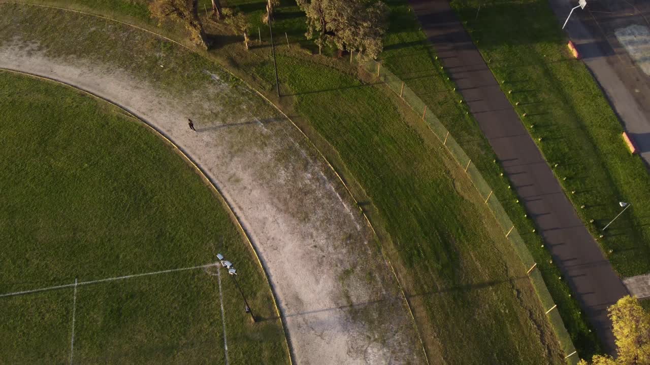 일몰에 축구장 주변을 뛰어다니는 사람의 공중 추적 샷 - 야외 훈련 세션 동안 선수의 4k 하향식