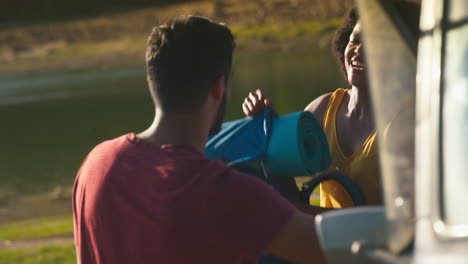 Couple-Unloading-Backpacks-From-Pick-Up-Truck-On-Road-Trip-By-Lake-In-Countryside