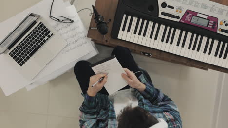 young male musician creating music and taking notes at home