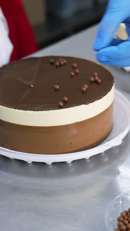 decoration of the cake at confectionary factory. worker puts white, milky and dark chocolate beads on top of the beautiful cake. close up. vertical video