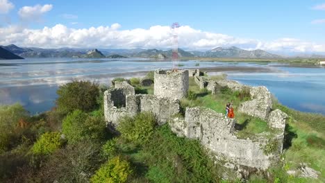 cellist plays in front of ancient castle ruins by the lake