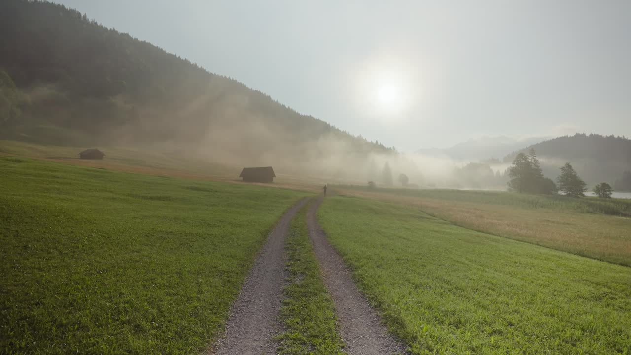 joven en forma corriendo hacia la cámara en un camino de campo al amanecer con niebla y sol, alemania