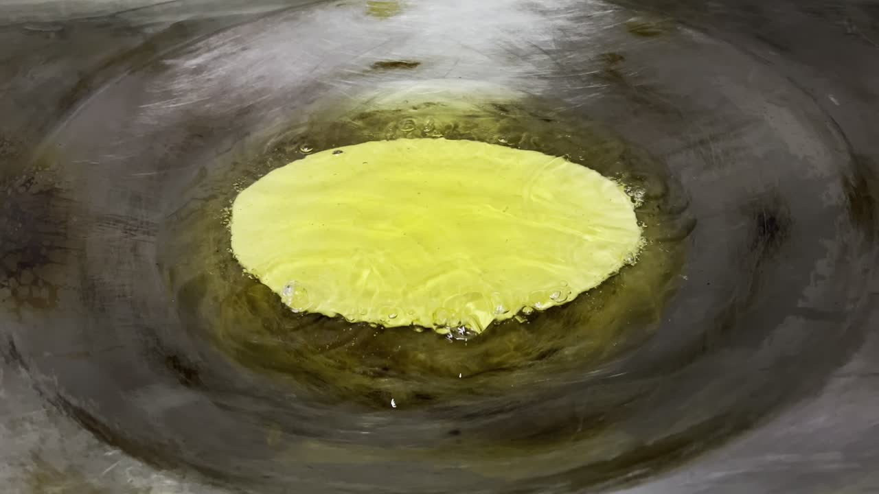 A thin layer of batter sizzles in hot oil on a large metal pan for a traditional dish