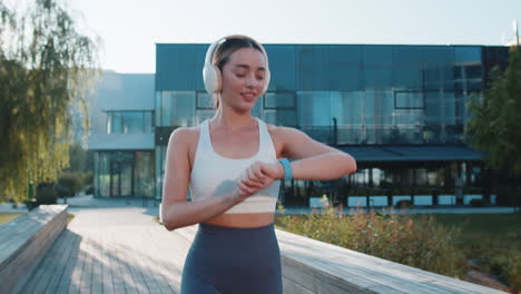happy athletic runner adult girl looks at smartwatch device fitness bracelet checking time in park