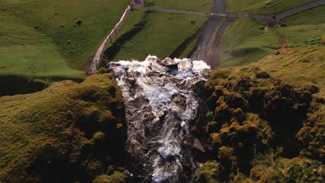 Powerful-waterfall-amidst-lush-green-landscape-with-misty-water-and-birds-soaring-in-the-sky,-shot-from-above