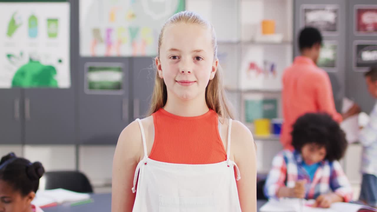 Ritratto di una felice scolaretta caucasica al banco con diversi alunni in un'aula scolastica.