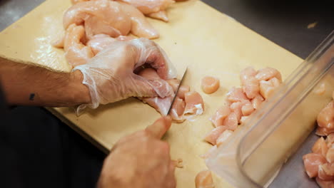 kitchen prep, dicing raw chicken breasts into chunks, cutting up poultry meat, slow motion close up 4k