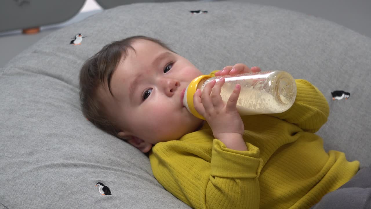 niño bebiendo leche de fórmula sosteniendo el biberón en ambas manos
