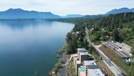 orbit drone shot of serene lake and winding road surrounded by lush forest and distant mountains on a clear day