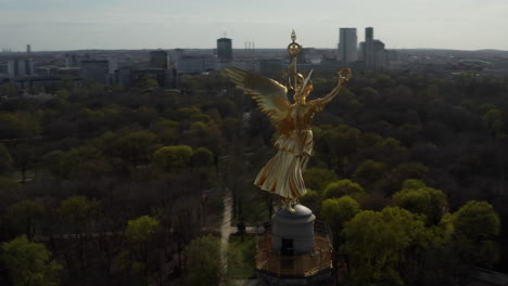 AERIAL:-Close-Up-Circling-around-Berlin-Victory-Column-Golden-Statue-Victoria-in-Beautiful-Sunlight-and-Berlin,-Germany-Cityscape-Skyline-in-Background