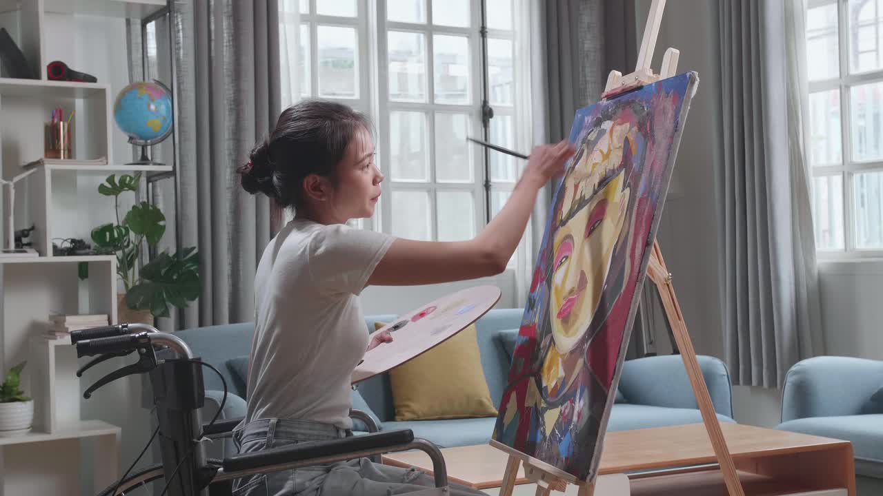 Talented Female Artist Sitting On Wheelchair, Enthusiastically Using Paint Brush She Creates With Oil Painting. Creative Studio With Canvas