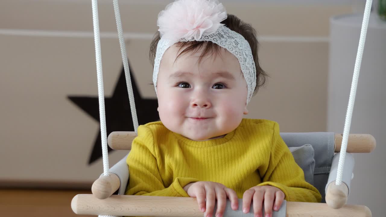 활과 노란색 스웨터를 입고 실내 출입구 스윙에 앉아 박수를 치는 행복한 아기 소녀