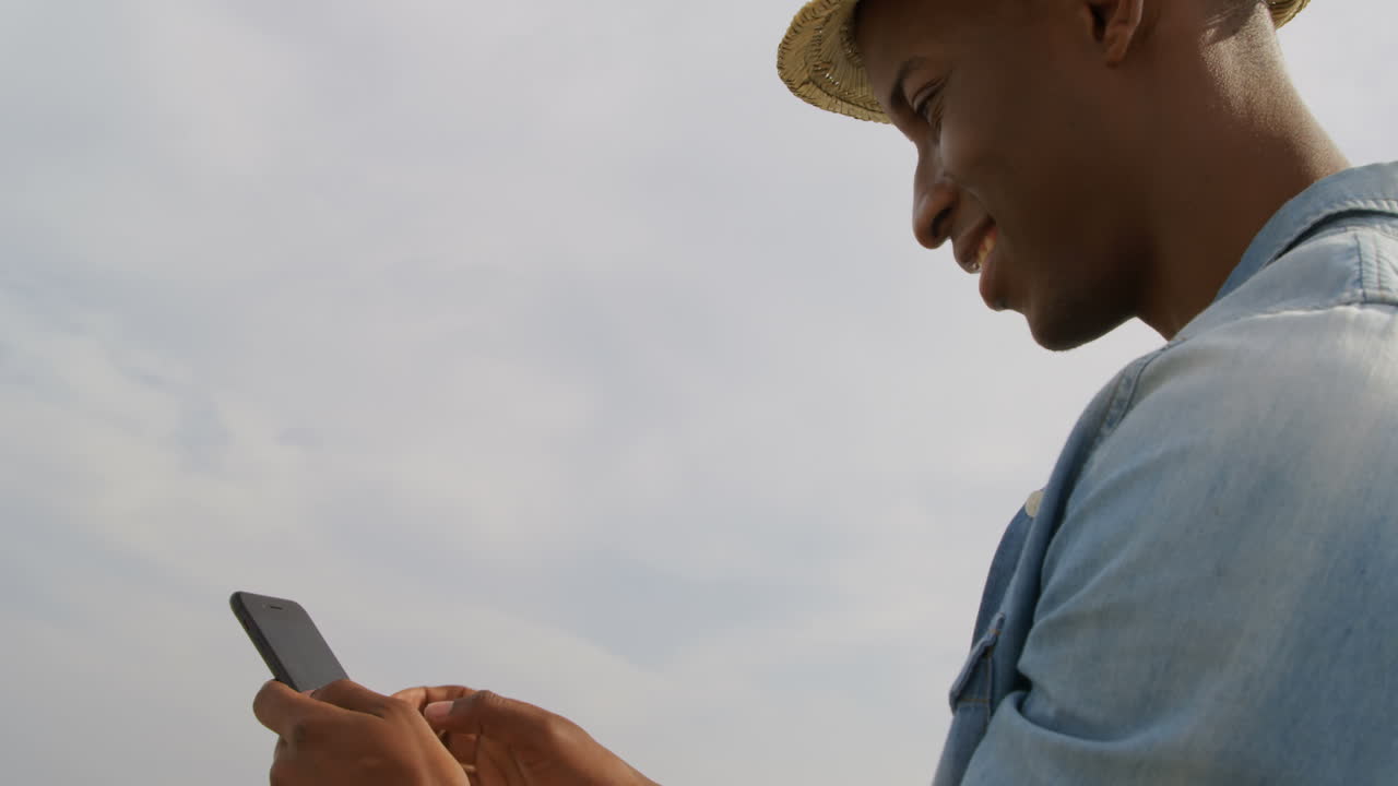 vista lateral de un hombre afroamericano usando teléfono móvil en la playa 4k