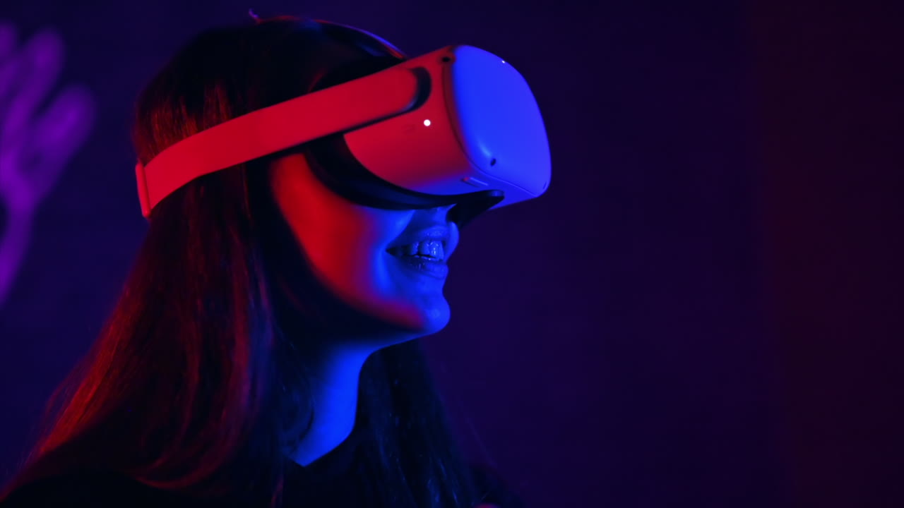 A young woman in VR glasses is smiling while playing VR games. Red and blue illumination. Slow motion
