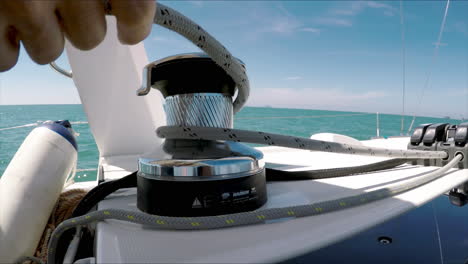 a hand releasing rope from a winch aboard a sailing yacht