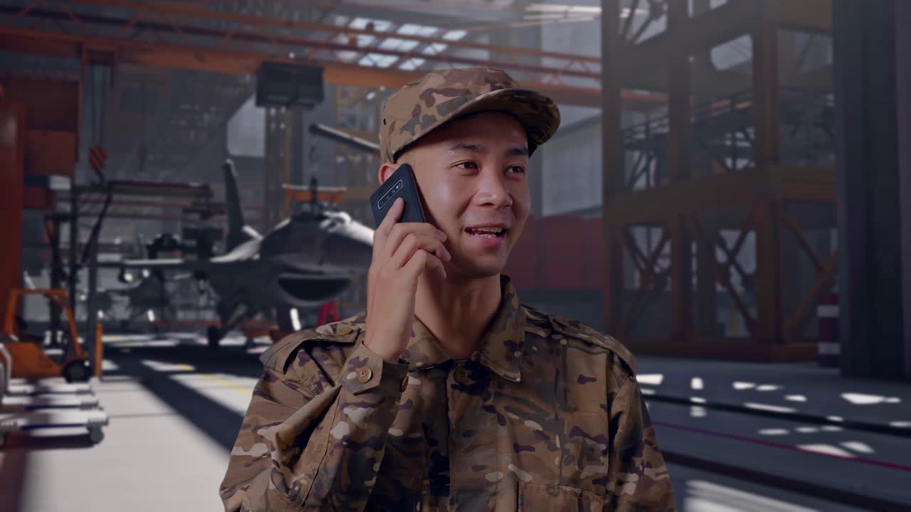 Soldato felice in uniforme mimetica che parla al telefono in un hangar