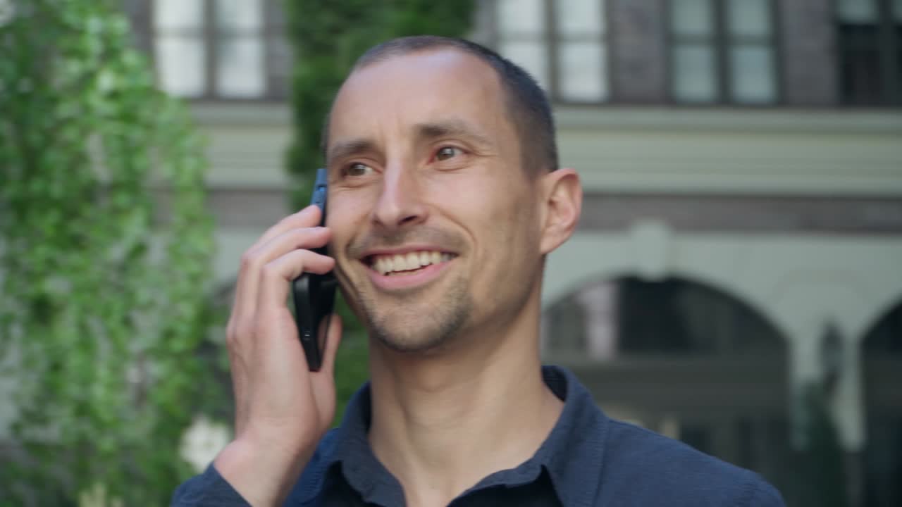 hombre joven de 4k de pie en la calle en el fondo de un edificio moderno hablando por teléfono