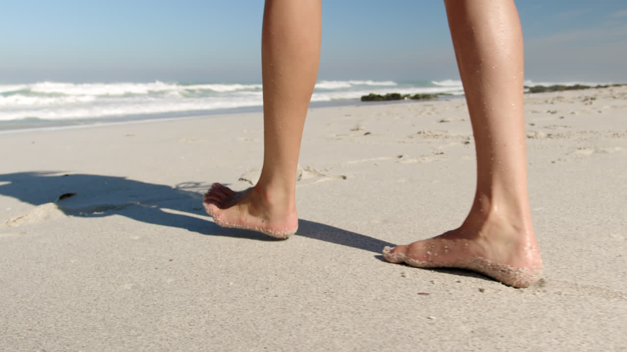 Giovane donna che cammina sulla spiaggia sotto il sole 4K