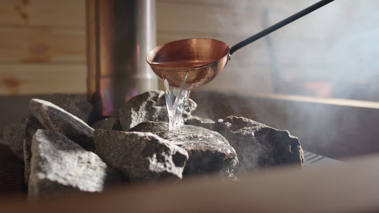 Steam rise from heated rocks as copper sauna ladle pours water on, closeup slomo