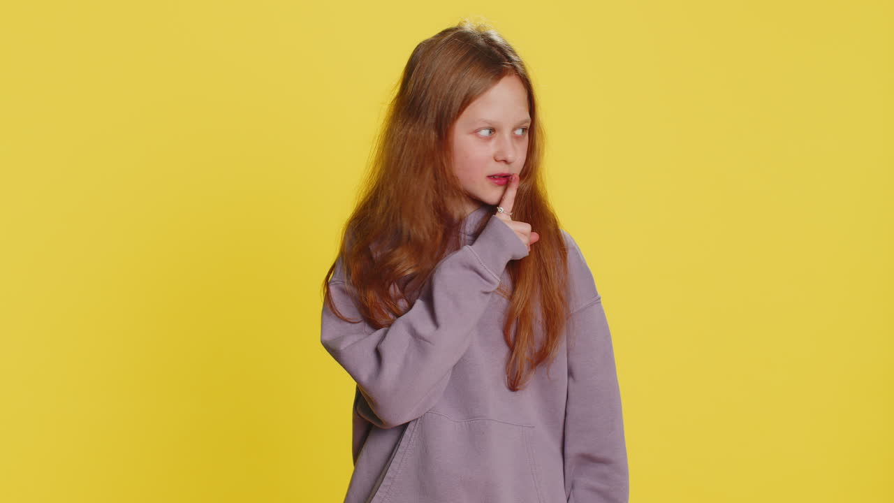 Preteen child girl presses finger to lips makes silence hush sign do not tells gossip secret quiet
