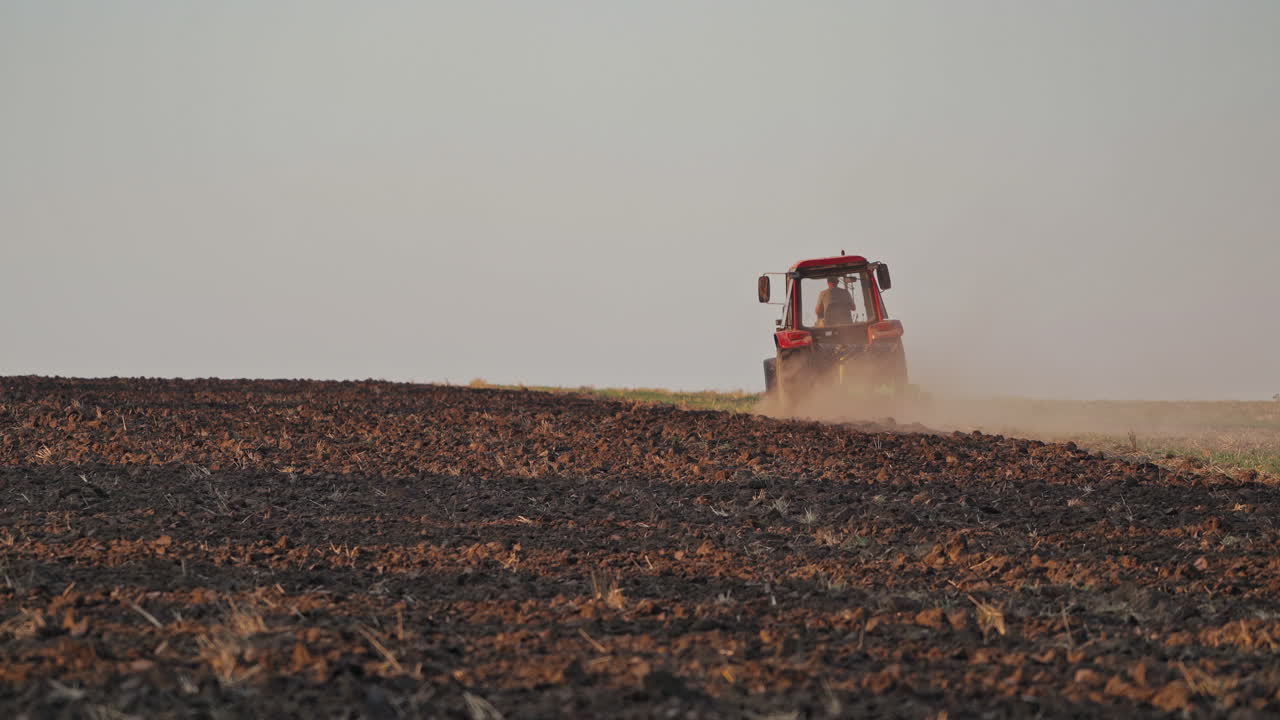 Brown field background and a tractor plowing the soil. Tractor cultivating the field, preparing land for sowing in the farmland.