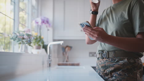un primer plano de una soldada estadounidense en uniforme en la cocina en casa con un teléfono móvil