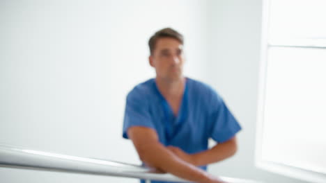 Portrait-Of-Thoughtful-Young-Male-Doctor-Or-Nurse-Standing-On-Stairs-In-Hospital