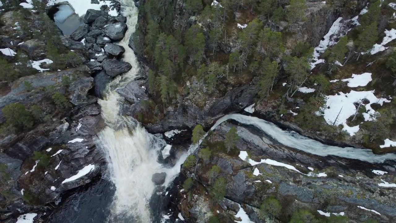 Una panoramica verso il basso rivela una cascata che scende attraverso un paesaggio montuoso e boscoso con fiume e scogliere rocciose in Norvegia.