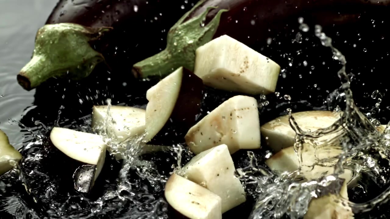 Melanzane fresche a cubetti che schizzano nell'acqua scura al rallentatore