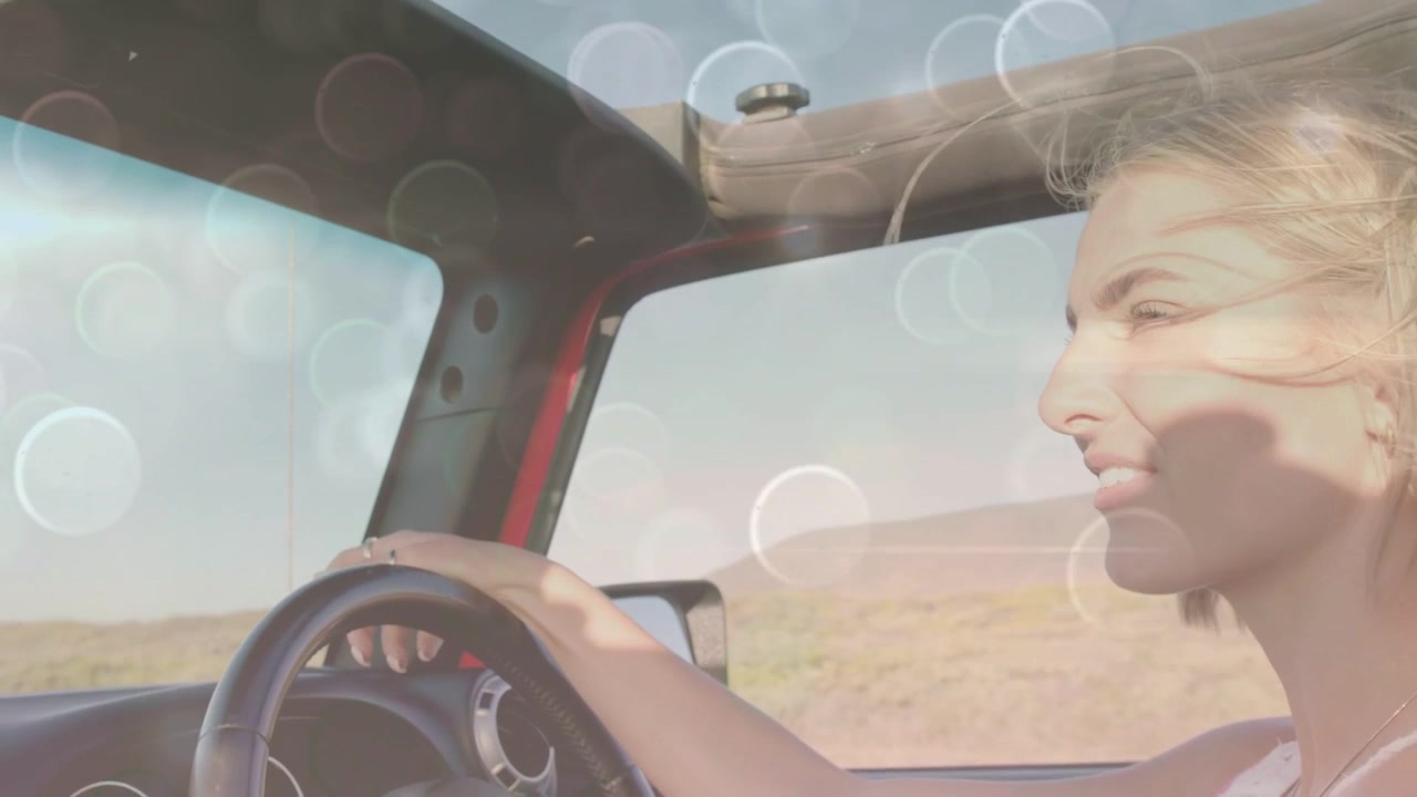 Donna che guida e sorride mentre la capote aperta lascia entrare il vento e il bokeh si ammorbidisce intorno al conducente per un viaggio