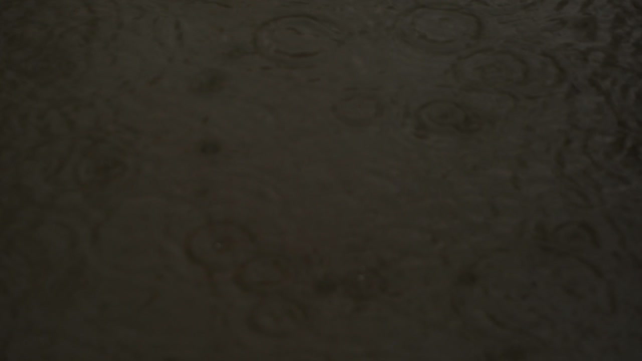 Abstract close-up of dark, rippled water surface in low light. Soft circular wave patterns and subtle liquid textures create a moody, minimalist organic background.
