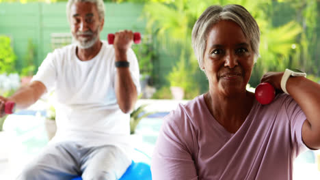 una pareja de ancianos haciendo ejercicio con pesas en casa.