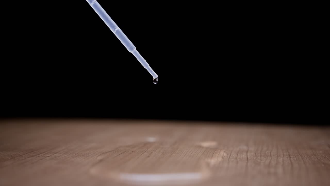 Dripping water drop from a pipette, super slow motion on wooden surface