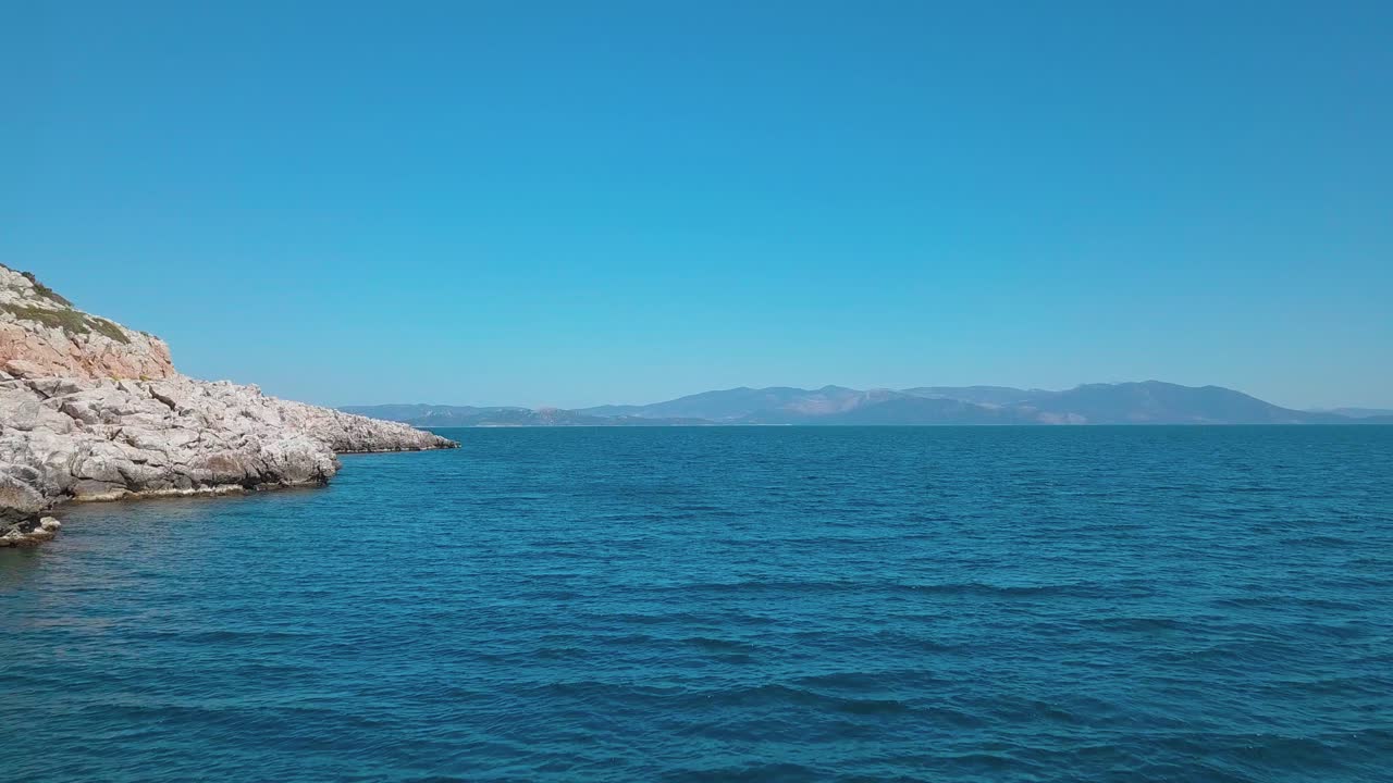 Forward low altitude aerial shot next to a rocky shore over the aegean sea with a view of Euvoia
