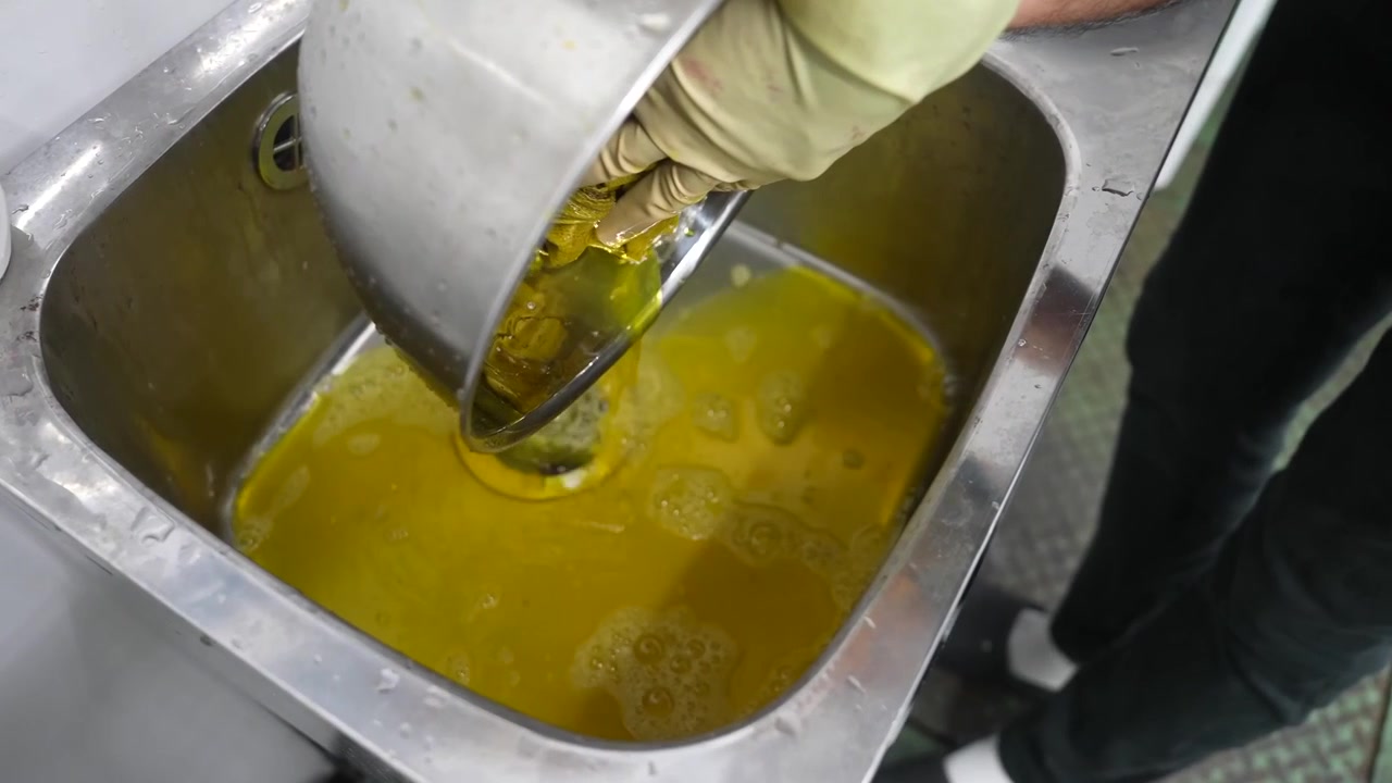 Trabalhador derrama mistura de corante amarelo em pia de processamento de aço inoxidável.