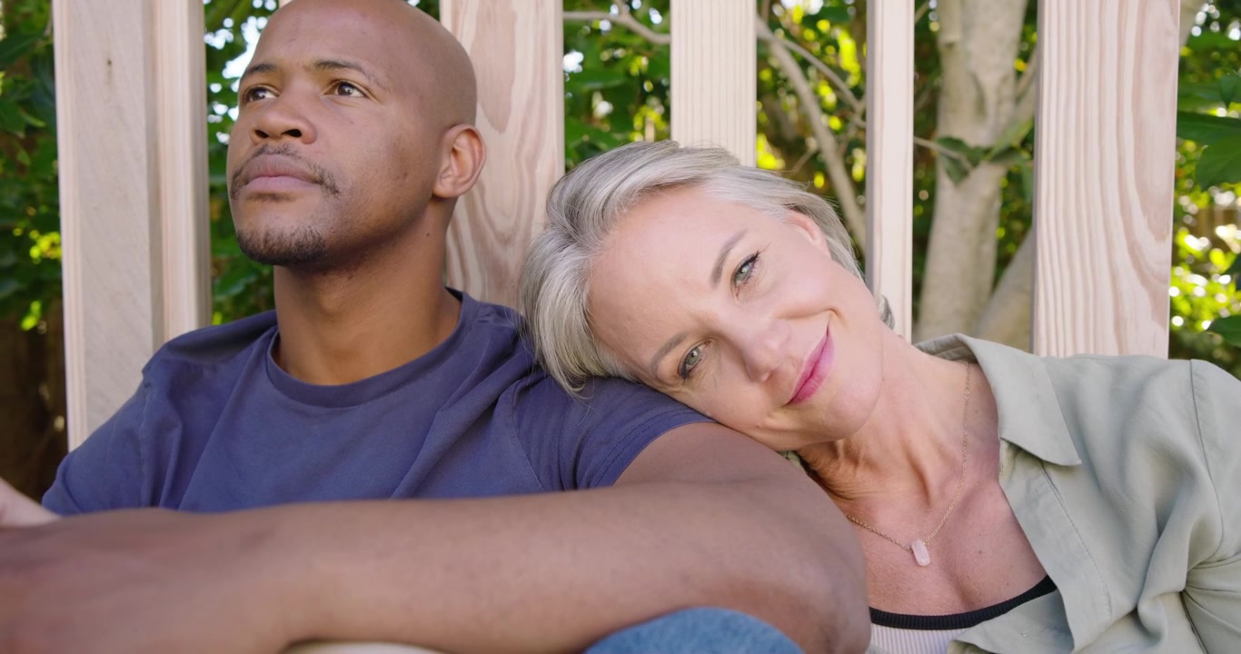 Coppia romantica seduta in veranda, la donna appoggia la testa, tenendo l'avambraccio, l'uomo guarda in alto, mostrando amore.