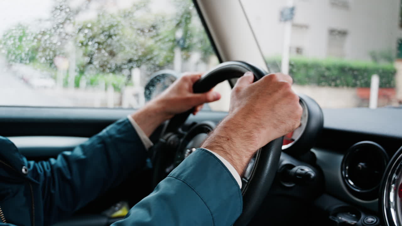 Close up of a man's hands on a steering wheel, driving a car on the road in the rain