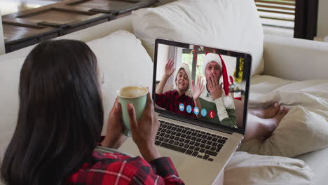 mujer biracial usando portátil en video chat con amigos durante la navidad en casa